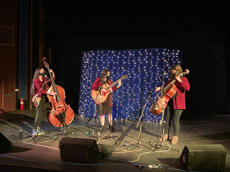 Image of three women playing standup base, guitar, and cello. 